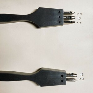 May include: Two black leather hole punch tools with wooden handles. The tools have multiple punch sizes and are used for creating holes in leather.