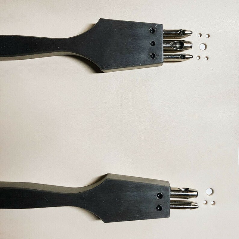 May include: Two black leather hole punch tools with wooden handles. The tools have multiple punch sizes and are used for creating holes in leather.