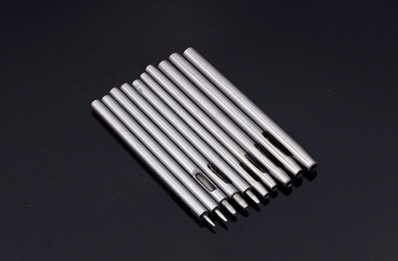 May include: Set of ten silver metal hole punch tools with different sized holes. The tools are arranged in order of size, with the smallest hole punch on the left and the largest hole punch on the right.