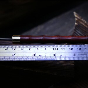 May include: A close-up of a wooden tool with a metal tip. The tool is about 5 inches long and has a dark brown finish. The tool is lying on a ruler with markings in inches and centimeters.