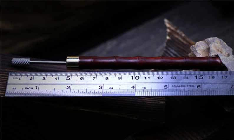 May include: A close-up of a wooden tool with a metal tip. The tool is about 5 inches long and has a dark brown finish. The tool is lying on a ruler with markings in inches and centimeters.