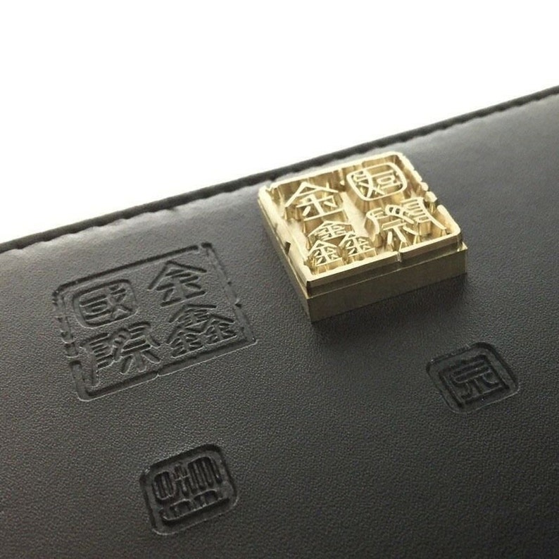 May include: A close-up of a black leather wallet with a gold embossed stamp. The stamp features the Chinese characters "金賞" which translates to "Gold Award".