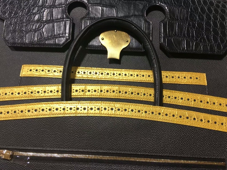 May include: Close-up of a black leather handbag with gold-colored straps. The straps have a repeating pattern of small circles.