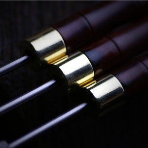 May include: Three wooden dowels with gold metal tips. The dowels are dark brown and have a smooth finish.