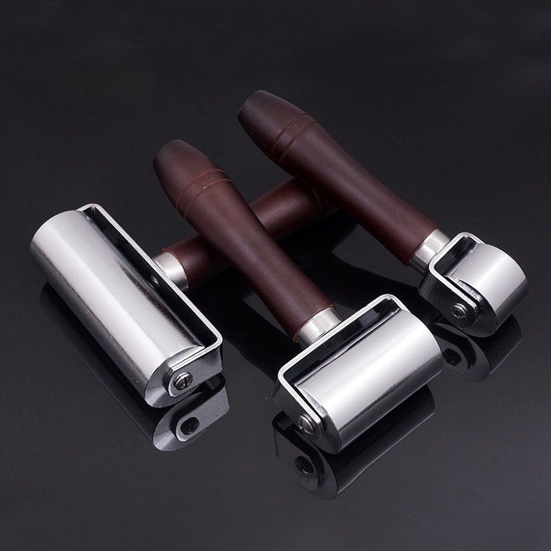 May include: Three leather working tools with brown wooden handles and silver metal rollers. The rollers are different sizes.