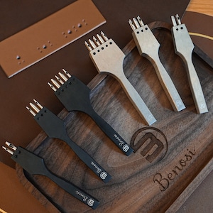 May include: Five leather hole punch tools with different sized punches on a wooden tray. The tray has the word "Benosi" engraved on it.