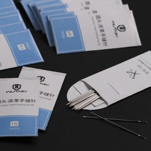 May include: A pack of 12 leather sewing needles, labeled "Round Head Leather Hand Sewing Needle" in English and Chinese. The needles are packaged in a white envelope with a red cross symbol.