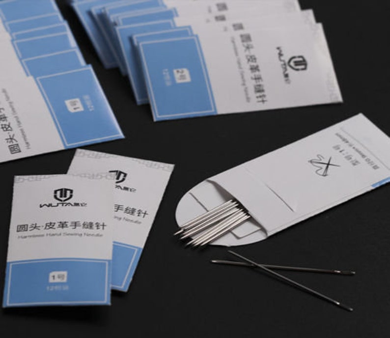 May include: A pack of 12 leather sewing needles, labeled "Round Head Leather Hand Sewing Needle" in English and Chinese. The needles are packaged in a white envelope with a red cross symbol.