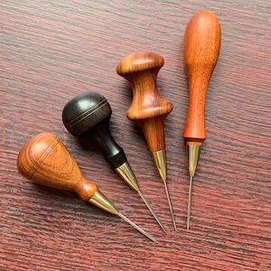 May include: Four leather sewing awls with wooden handles. The awls have brass tips and are used for hand-stitching leather.