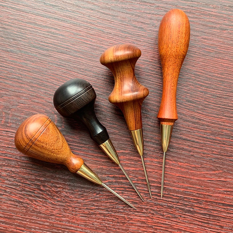 May include: Four leather sewing awls with wooden handles. The awls have brass tips and are used for hand-stitching leather.