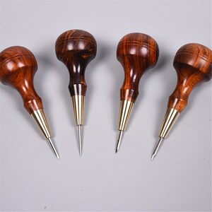 May include: Four wooden awls with brass tips. The awls have a rounded wooden handle and a pointed metal tip. The awls are used for leather crafting.
