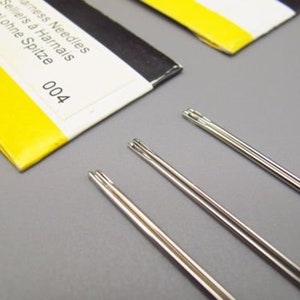 May include: Three silver sewing needles with no point, labeled "Stainless Needles Sellers &agrave; Harnais Aiguille ohne Spitze 004".