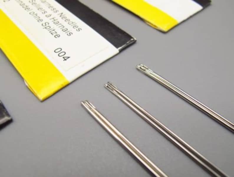 May include: Three silver sewing needles with no point, labeled "Stainless Needles Sellers &agrave; Harnais Aiguille ohne Spitze 004".