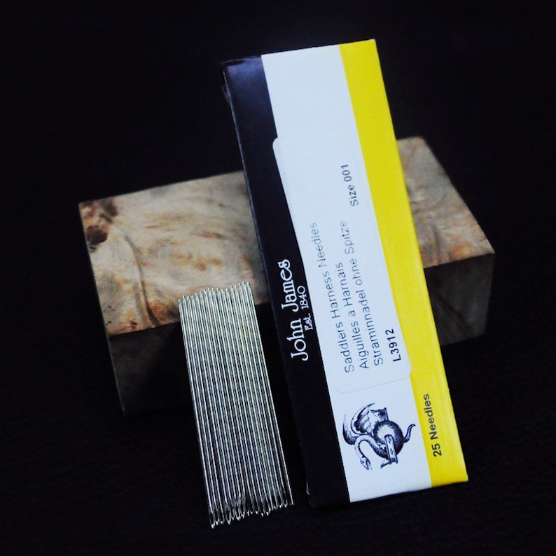 May include: A pack of 25 silver saddlers harness needles, size 001, by John James, Est. 1840. The needles are packaged in a black and yellow box with the brand name and product information printed on it.