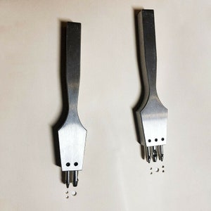 May include: Two metal leather hole punch tools with multiple prongs. The tool on the left has three prongs and the tool on the right has five prongs.