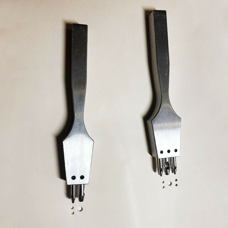 May include: Two metal leather hole punch tools with multiple prongs. The tool on the left has three prongs and the tool on the right has five prongs.