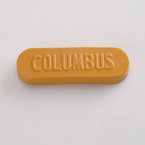 K&ouml;nnte beinhalten: Ein langes, rechteckiges, goldgelbes Wachssiegel mit dem Wort "COLUMBUS" in der Mitte gepr&auml;gt.