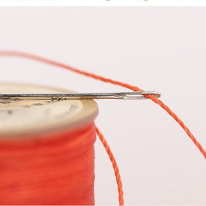 May include: A spool of bright orange thread with a needle threaded through it.