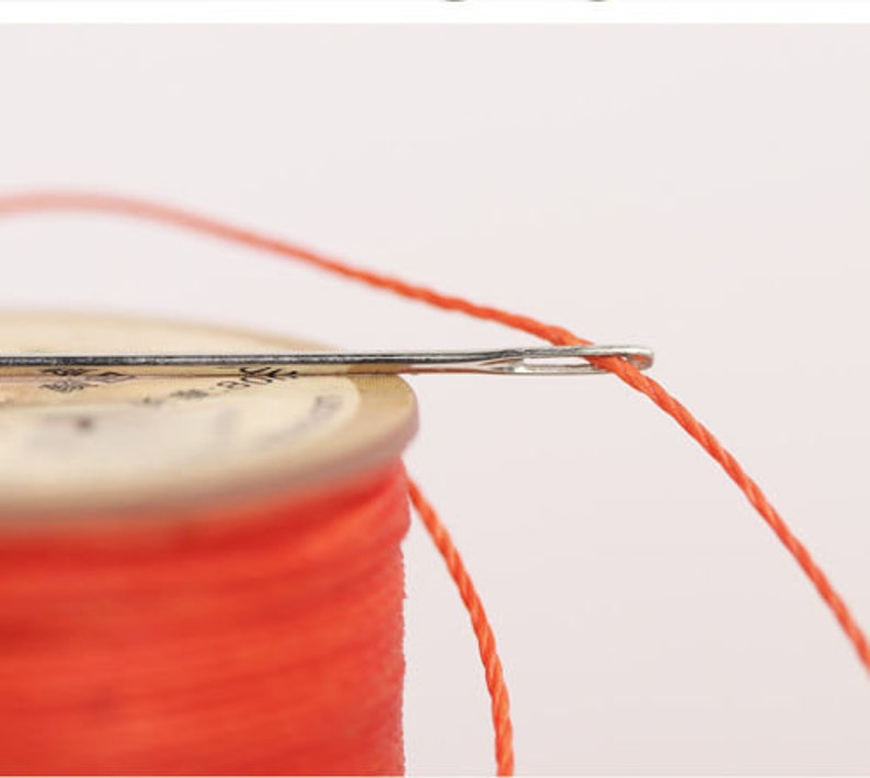 May include: A spool of bright orange thread with a needle threaded through it.