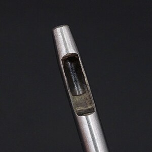 May include: Close-up of a silver metal punch tool with a round, hollow opening.