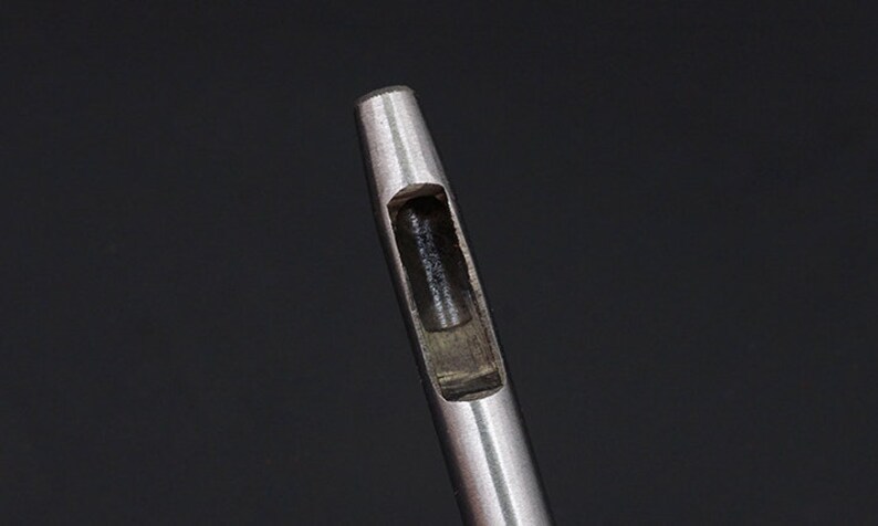 May include: Close-up of a silver metal punch tool with a round, hollow opening.