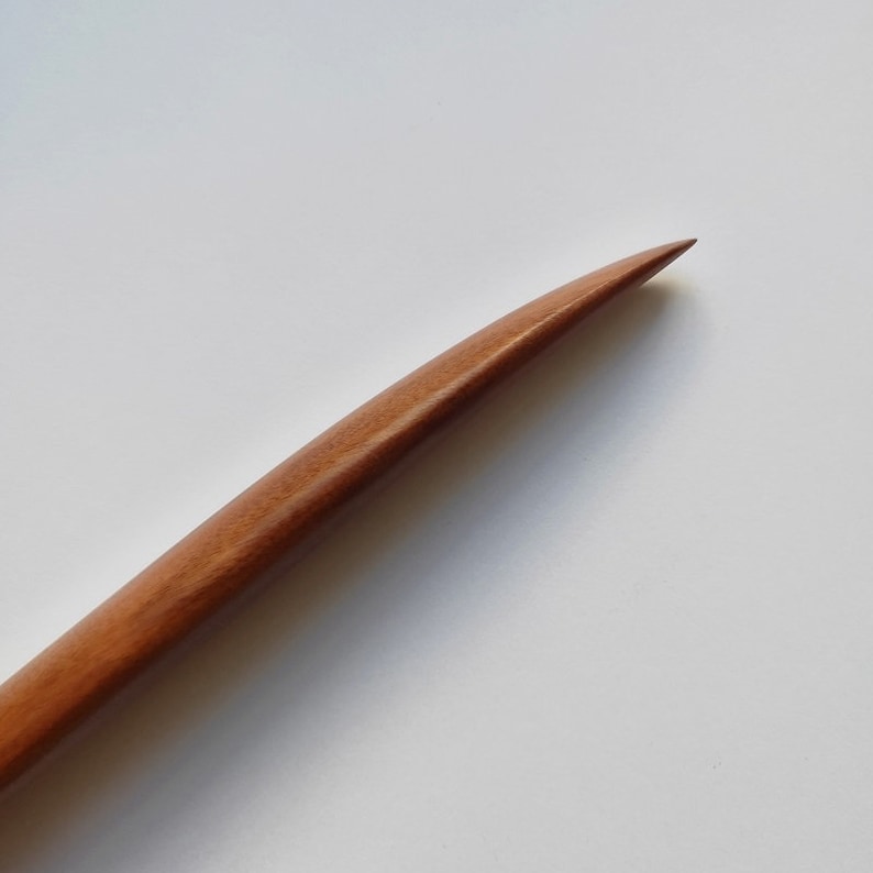 May include: A close-up of a wooden tool with a pointed tip. The tool is made of light brown wood and has a smooth, polished finish.