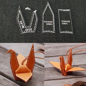 May include: Three clear plastic templates for leather crafting. The templates are labeled with the text "A01X2", "XKB-213 A02X1", and "XKD-S12 AXEDA". The templates are used to create a leather origami crane.