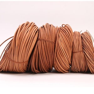 May include: Four spools of brown leather cord, varying in thickness, are arranged in a row. The cords are tightly wound and have a natural, rustic look.