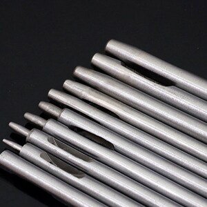 May include: A set of ten silver metal hole punches of varying sizes. The punches are arranged in a fan shape, with the smallest punch at the bottom and the largest punch at the top.