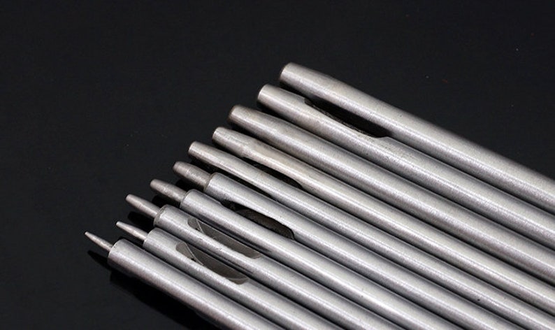 May include: A set of ten silver metal hole punches of varying sizes. The punches are arranged in a fan shape, with the smallest punch at the bottom and the largest punch at the top.
