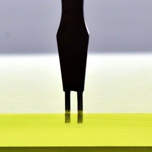 May include: A black tool with two prongs is inserted into a yellow surface.