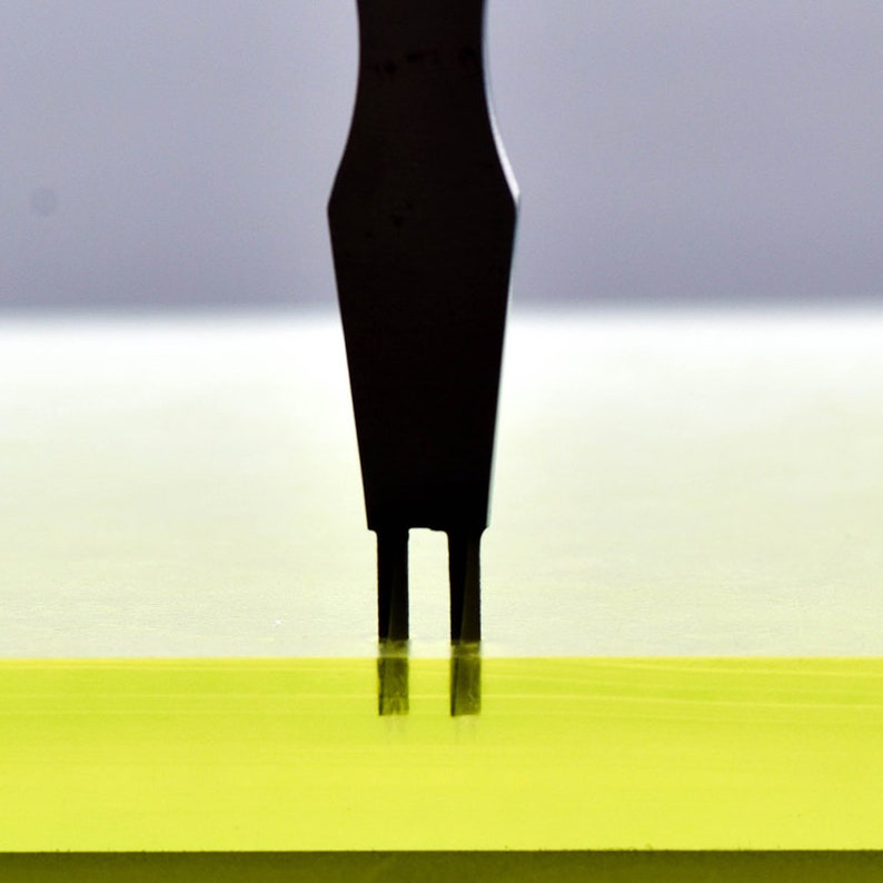 May include: A black tool with two prongs is inserted into a yellow surface.