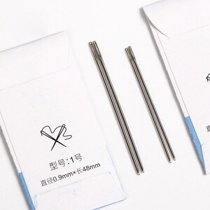 May include: A pack of four silver sewing needles, with a white label that reads "型号: 1号 直径0.9mm&times;长48mm".
