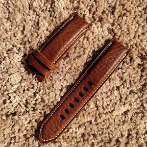 Pu&ograve; includere: Due cinturini per orologio in pelle marrone con cuciture bianche. Il cinturino a sinistra ha un design semplice, mentre il cinturino a destra ha pi&ugrave; fori.
