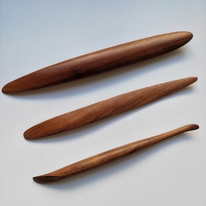 May include: Three wooden tools for pottery, made of dark brown wood. The tools are different sizes and shapes, with rounded ends.
