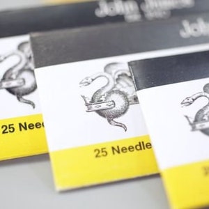 May include: Three packages of sewing needles with a yellow label and a black and white illustration of a dragon. The label reads "25 Needles".