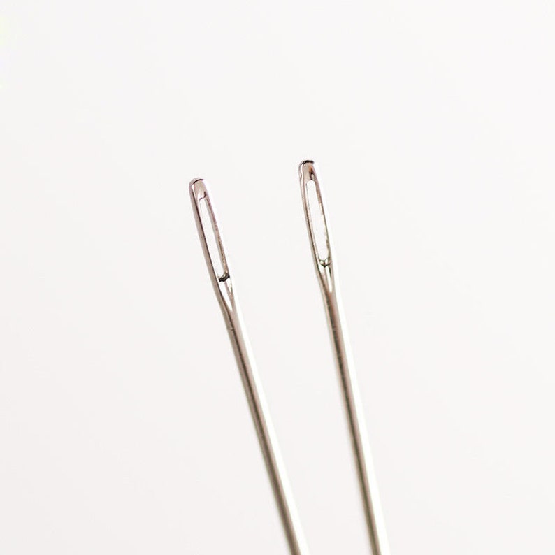 May include: Two silver sewing needles on a white background.