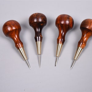 May include: Four wooden awls with brass ferrules and sharp steel points. The awls have a dark brown wood finish and are arranged in a row on a grey surface.