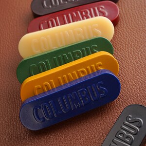K&ouml;nnte beinhalten: Sechs Schuhputzstift in verschiedenen Farben, darunter Schwarz, Rot, Gelb, Gr&uuml;n und Blau. Jeder Stift ist mit "COLUMBUS" beschriftet.