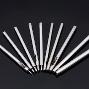 May include: A set of ten silver metal hole punches of varying sizes, arranged in a fan shape on a black surface.