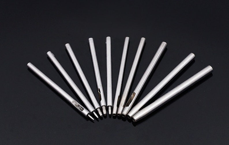 May include: A set of ten silver metal hole punches of varying sizes, arranged in a fan shape on a black surface.