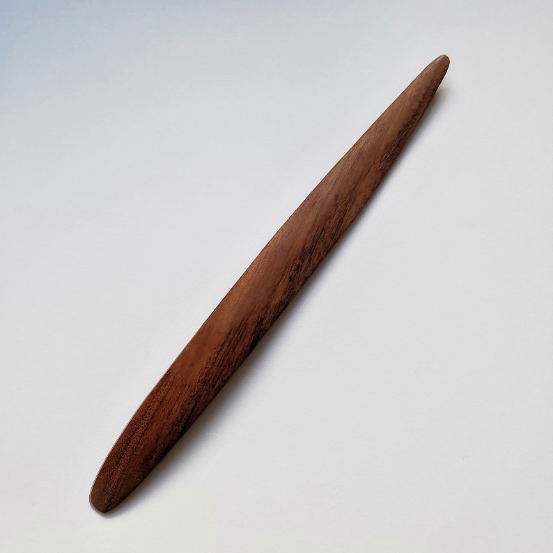 May include: A long, thin, wooden letter opener with a rounded tip. The letter opener is made of dark brown wood with a natural grain pattern.