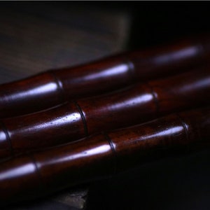May include: Three dark brown wooden sticks, possibly bamboo, are stacked on top of each other. The sticks are smooth and polished, with a slight sheen.