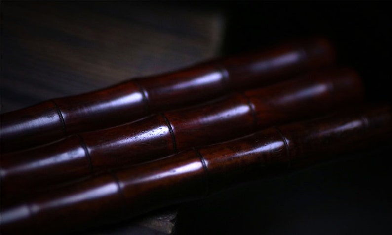 May include: Three dark brown wooden sticks, possibly bamboo, are stacked on top of each other. The sticks are smooth and polished, with a slight sheen.