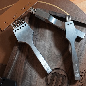 May include: Two silver leather hole punch tools with wooden handles. The tools are labeled "Benechi" and have different sized punch heads.