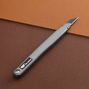May include: A gray retractable utility knife with a silver blade. The knife has a red and white label that reads "SDI NO. 3006" and the words "BLADE CHANGE" are printed on the blade.