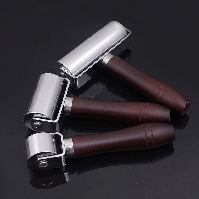 May include: Three silver leather rollers with brown wooden handles. The rollers are used for pressing leather and other materials.