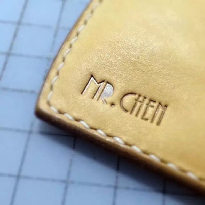 May include: Close-up of a light brown leather wallet with white stitching. The wallet has the name "MR. CHEN" embossed in the leather.