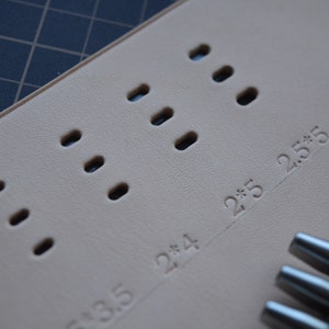 Pu&ograve; includere: Primo piano di una superficie in pelle marrone chiaro con pi&ugrave; fori rotondi punzonati in un motivo. La superficie &egrave; contrassegnata dai numeri "2*3.5", "2*4" e "2*5.5".