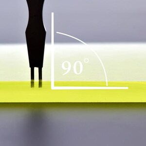 May include: A black tool with two prongs is being used to test the 90 degree angle of a yellow surface.